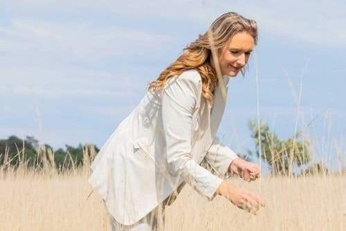 Zelfverzekerd in je energie – persoonlijke groei met Human Design Vrouw staat krachtig en energiek in rietveld, symbool voor zelfvertrouwen en persoonlijke groei.