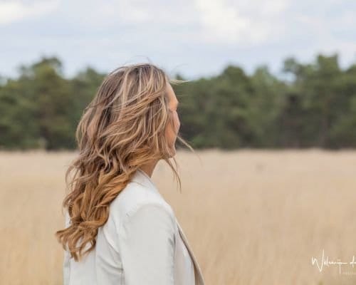Zelfverzekerd in je energie – persoonlijke groei met Human Design Vrouw staat krachtig en energiek in rietveld, symbool voor zelfvertrouwen en persoonlijke groei.