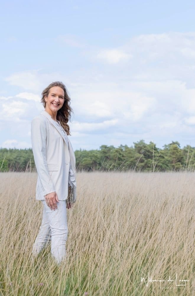 Vrouw staat krachtig en energiek in rietveld, symbool voor zelfvertrouwen en persoonlijke groei.